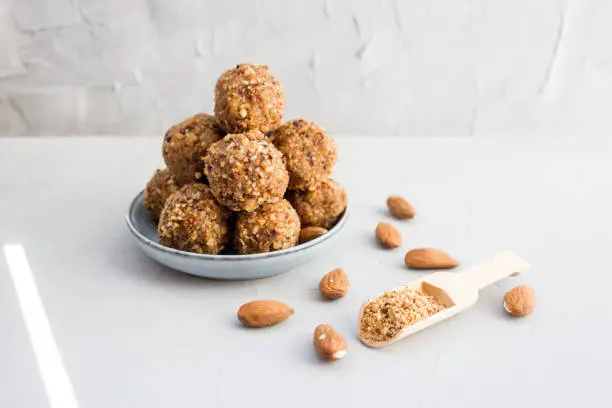 Organic healthy energy balls of dates, peanuts, honey, almonds in walnut chips on a light background, copy the space, lie flat. Healthy food, healthy snack. Raw dessert. Gray background.