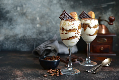 Tiramisu - traditional italian dessert with mascarpone cheese, biscuit and coffee in a glasses on a dark background.