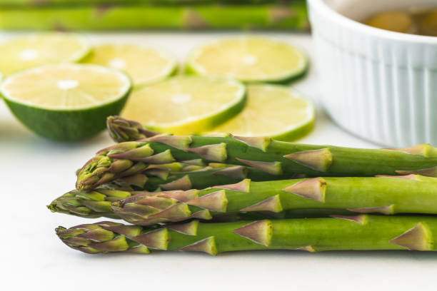 Green asparagus, sliced lemon, olive oil close up on marble serving board on white background