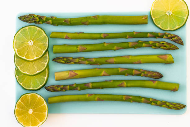 Asparagus and sliced lemon close up on blue serving board on white background, view from above