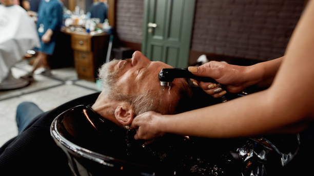 istock Before doing haircut. Handsome mature bearded man keeping eyes closed and relaxing while barber washing his hair in the modern barbershop or salon 1224052306