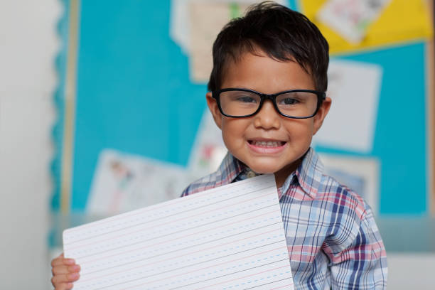 A little boy with a cute smile who is holding up a writting guide board and is wearing reading glasses with a preppy style shirt. stock photo