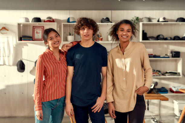 istock We do it right. Portrait of smiling workers looking at camera while standing in the office. Young man and two women working at custom T-shirt, clothing printing company 1224056085