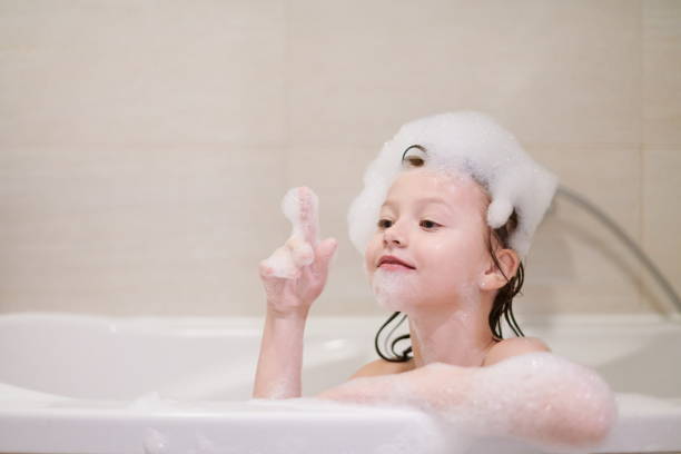 little girl in bath playing with soap foam little girl playing with soap foam in bath during coronavirus stay at home pandemic quarantine girls bath stock pictures, royalty-free photos & images