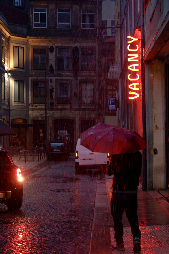 A person with an orange umbrella is walking in the rain under the bright neon sign