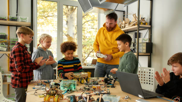 istock High performance. Young creative male teacher explains for students the principle of robotic machines work while holding console controller. Science and education. 1224063925