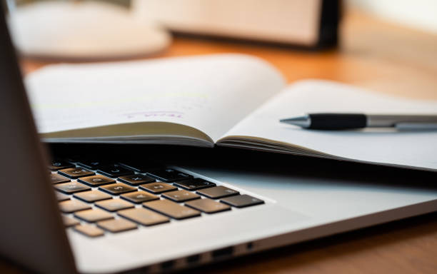 laptop-computer auf einem modernen business desk aus holz mit notizblock und stift im unfokussierten hintergrund. - pen and paper stock-fotos und bilder