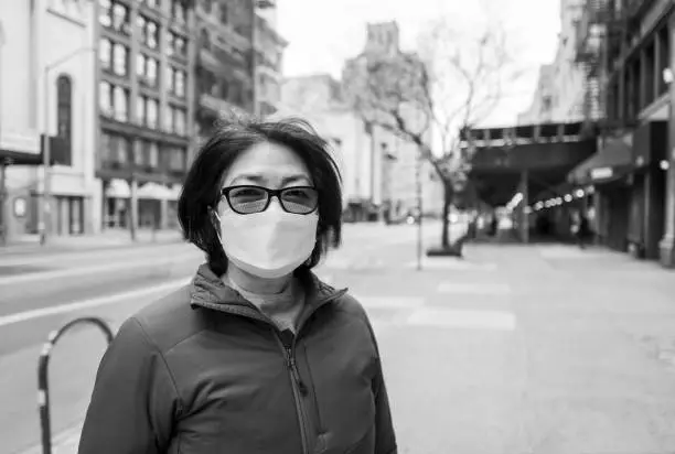 Senior Asian woman wearing surgical mask and practicing social distancing on the sidewalks of New York City during coronavirus pandemic.