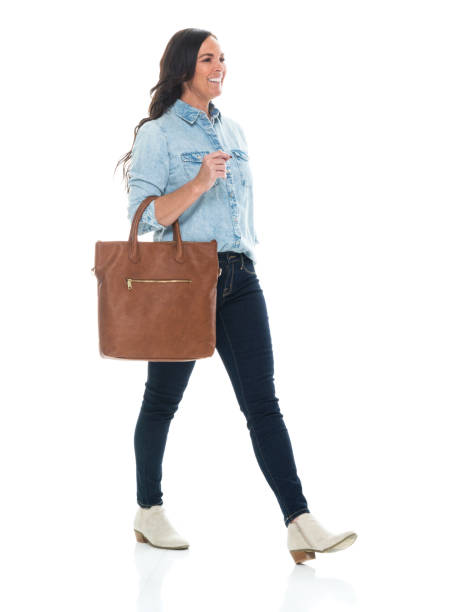 caucasian mid adult women walking in front of white background wearing shirt and holding purse - ações de bolsa imagens e fotografias de stock