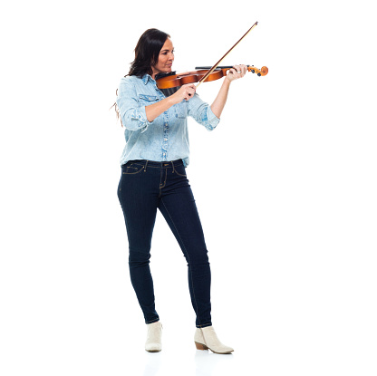 Front view of aged 40-44 years old who is beautiful with brown hair caucasian young women violinist standing in front of white background wearing pants who is laughing and holding violin