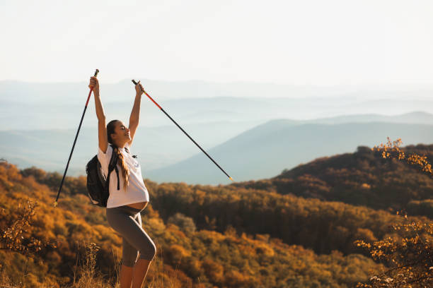 schwangere frau nordic walking mit trekkingstöcken auf hügeligem hügel mit herrlichem herbstblick. schwangerschaftsaktivität und gesunder lebensstil in der mutterschaftszeit. reisekonzept. - power walken stock-fotos und bilder