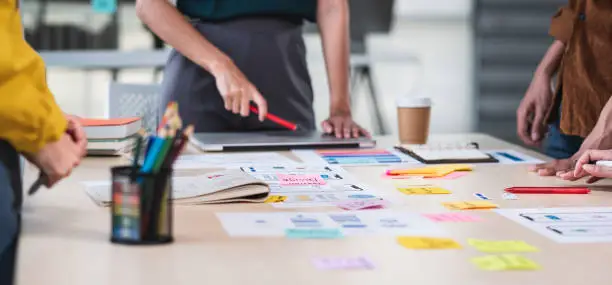Photo of Close up ux developer and ui designer brainstorming about mobile app interface wireframe design on table with customer brief and color code at modern office.Creative digital development agency.panning
