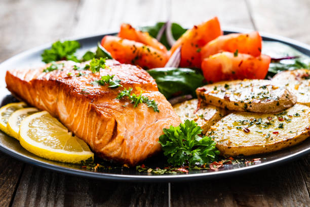 istock Fried salmon steak, fried potatoes and vegetables on wooden background 1224093133