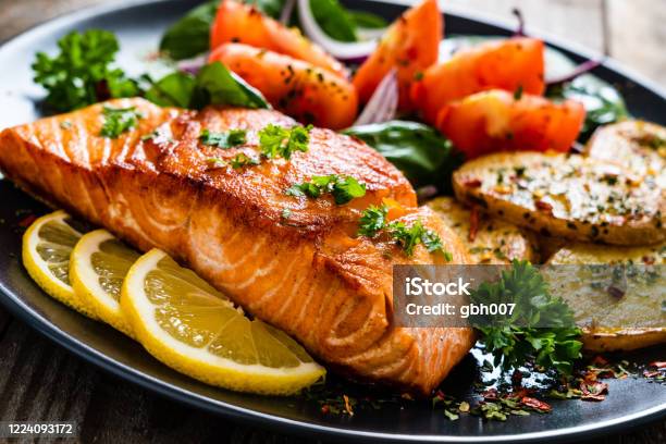 Fried Salmon Steak Fried Potatoes And Vegetables On Wooden Background Stock Photo - Download Image Now