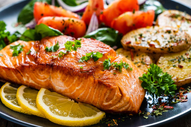 istock Fried salmon steak, fried potatoes and vegetables on wooden background 1224093194