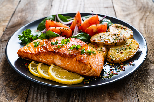 Barbecued salmon, fried potatoes and vegetables on wooden background