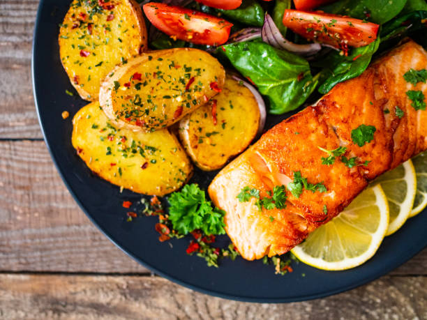 istock Fried salmon steak, fried potatoes and vegetables on wooden background 1224093269