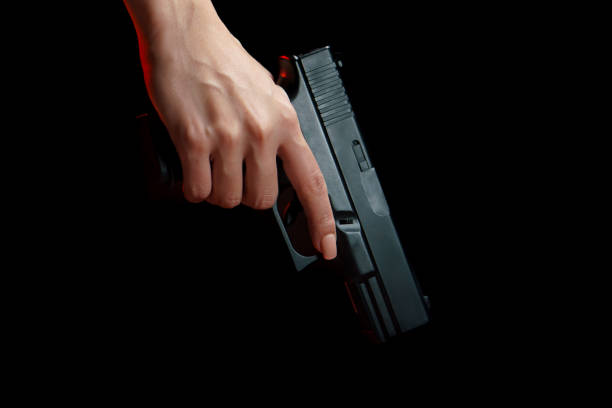 istock Woman holding a gun side him on black background. 1224095340