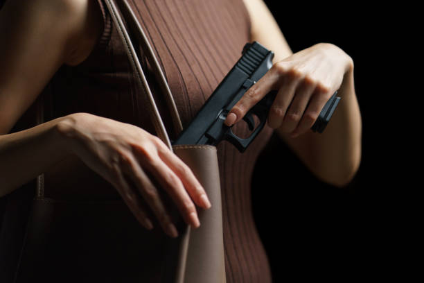 istock Woman hand pulling a pistol out of handbag on black background. 1224095411