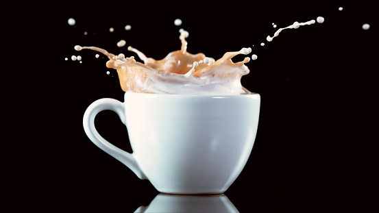 A cup with a large splash of coffee, isolated on black background