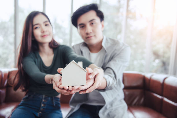 Couple Hands Holding Housing Model for Future Real Estate Saving, Attractive Asian Couple Hand Joint to Protection Home Property Togetherness. House Insurance and Residential Loan Investment Concept. Couple Hands Holding Housing Model for Future Real Estate Saving, Attractive Asian Couple Hand Joint to Protection Home Property Togetherness. House Insurance and Residential Loan Investment Concept. Joint Ownership Of Property stock pictures, royalty-free photos & images