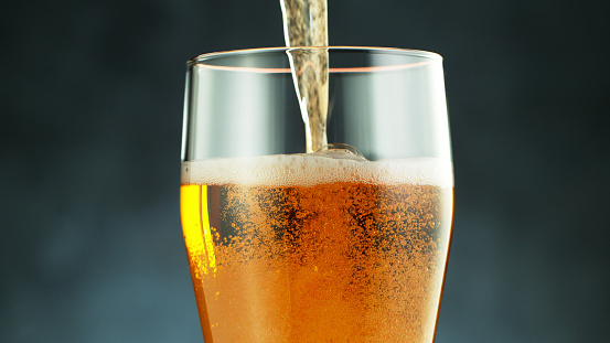 Close up of a wet pint of cold pale beer pouring, upper part of glass, dark background