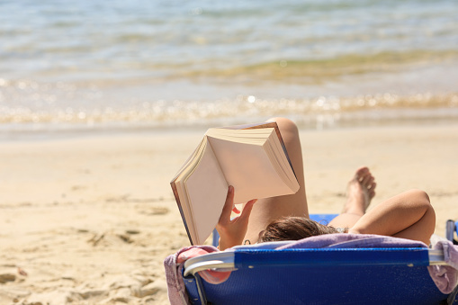 Beach holiday Young woman reading book, sunbathe, Relaxation at the sandy beach by the sea or ocean.