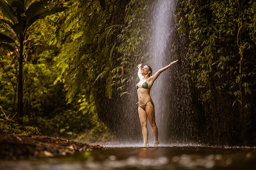 Happy woman enjoying under the waterfall in rainforest.