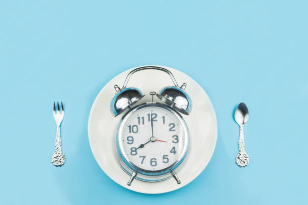 istock The old silver clock rests on a white plate. With a spoon and fork next to it on blue background,Eating on time concept 1224106272