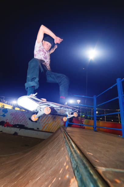 a young skater at night in a skatepark does the trick on the railing. x-ray culture nightlife concept - rolling up flash imagens e fotografias de stock