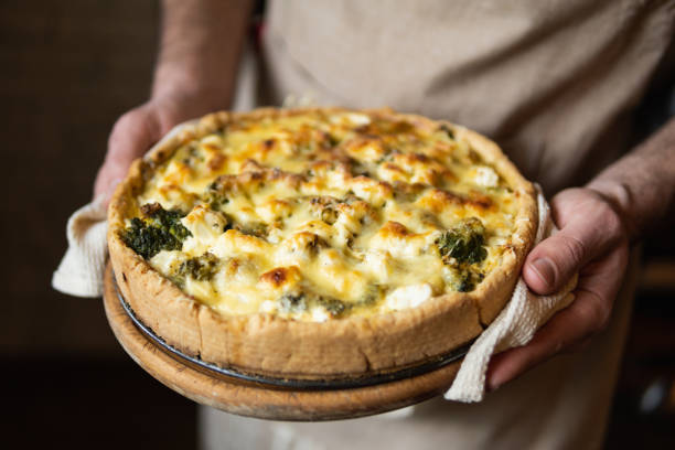 Male hands holding cheese and broccoli quiche tart. Home cooking according to French recipe stock photo