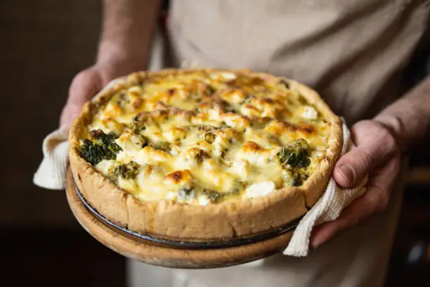 Male hands holding cheese and broccoli quiche tart. Home cooking according to French recipe.