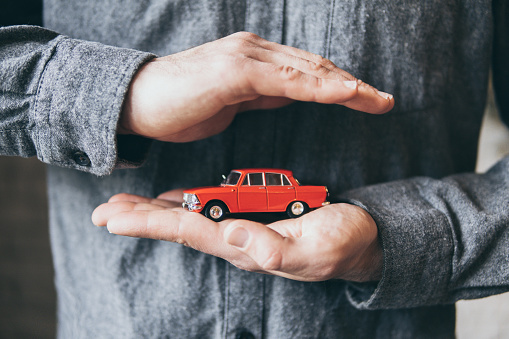 Male hands holding and protecting a red toy car. Conceptual image of insurance and road safety.