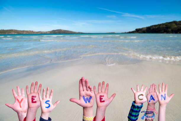 Children Hands Building Colorful Word Yes We Can. Ocean And Beach As Background