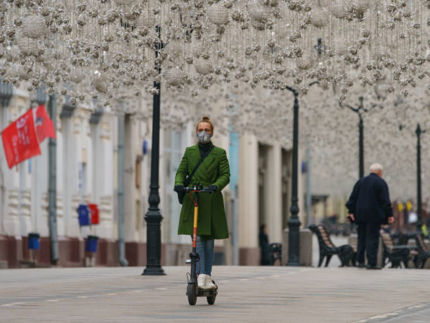 Moscow, Ruaaia - May 9, 2020: The celebration of the Victory day in the coronavirus pandemic time. Holidays in protective face mask. Young woman riding electric push scooter at Nikolskaya street.