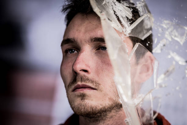 Close-up of broken glass pieces shattering on man's face.