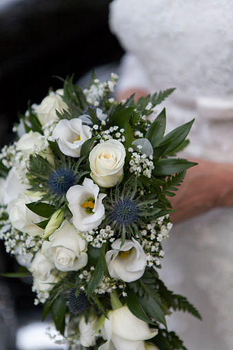 Close-up of a bride's hands holding a bouquet of flowers containing thistles and white roses