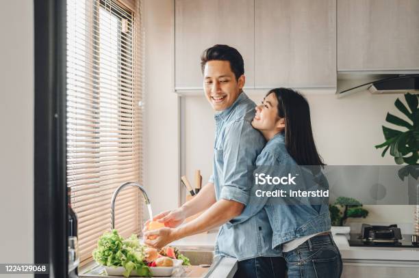 Asian Couple Lovers Hug In The Kitchen While Cooking At Home Stock Photo - Download Image Now