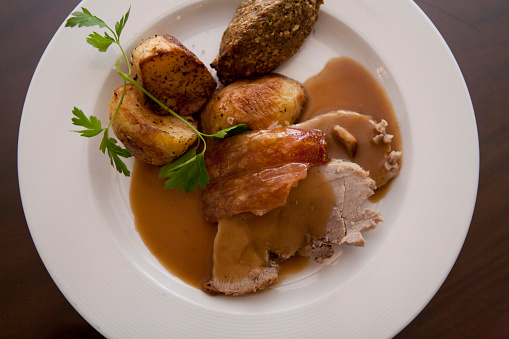 Overhead view of roast pork, roast potatoes, stuffing and gravy on a plate