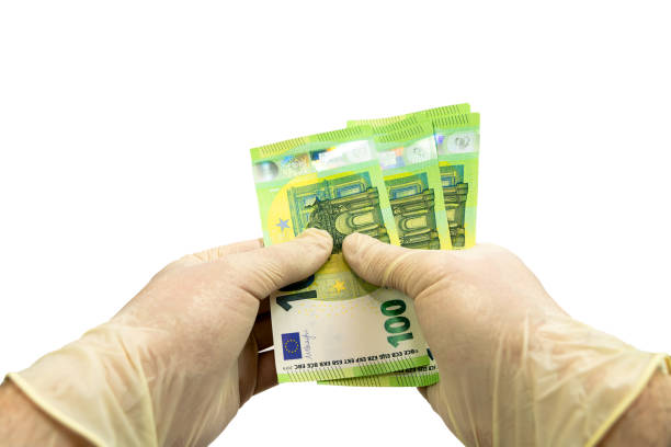 istock Two hands in white protective gloves hold a bundle of 100 Euro bills. Isolated white background. Virus protection concept. 1224135563