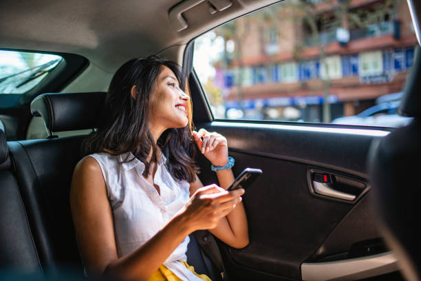 Young Female Vacationer with Smart Phone in Backseat of Taxi Interior view of Indian female tourist in mid 20s holding smart phone and looking out window in backseat of taxi. happy car asian stock pictures, royalty-free photos & images