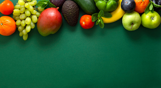 Fresh fruits frame and vegetables over green background, copy space.