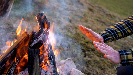 Close up of mature man warming his hands over campfire at dusk.