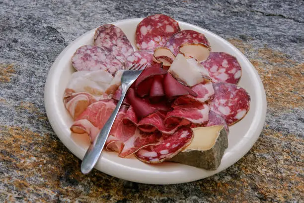 Typical authentic variety of processed cold meat products and mountain goat cheese on a white plate, Ticino, Switzerland, Europe. This kind of cold plate is also seen in Italy