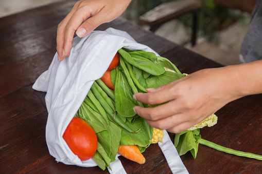 Close up shot of Asian woman buying fresh vegetables with reusable grocery tote bag during Covid 19 pandemic