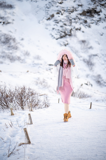 Asian Woman in winter clothes walking on a road surrounded by snow. In winter Iceland