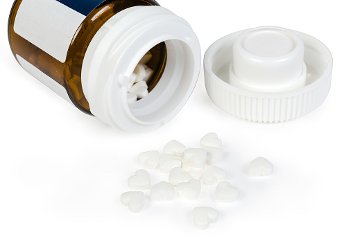 White heart shaped pills against the brown glass pill bottle with open lid on a white background