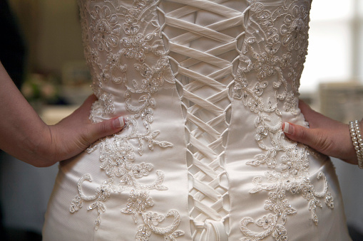 Straight view of the back of a wedding dress with the bride's hands o her hips
