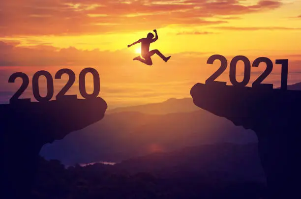 Silhouette man jump between 2020 and 2021 years with sunset background, Success new year concept.
