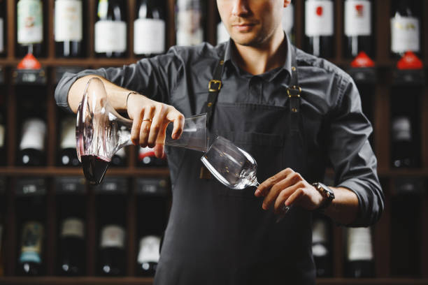 istock Bartender pours red wine in glass from big transparent vessel 1224141879